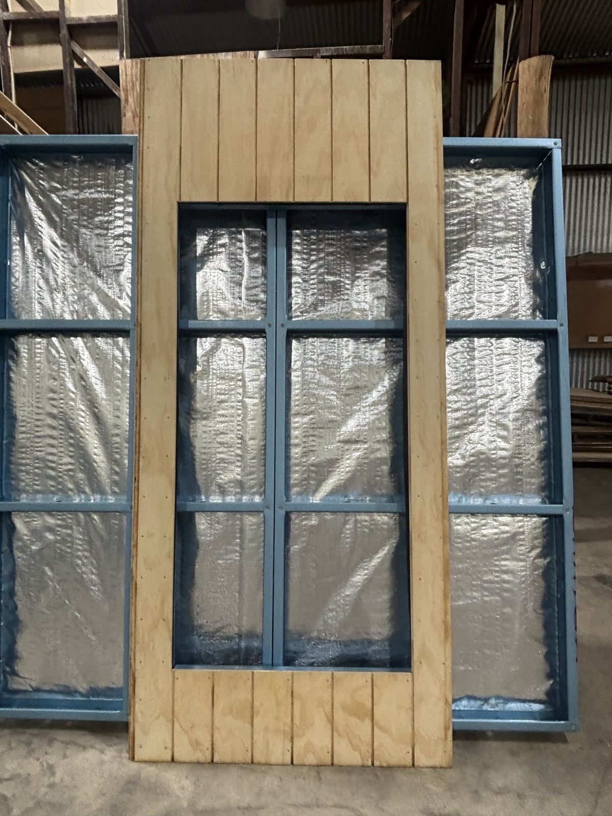 A clad panel with a framed window opening and foil wrap behind